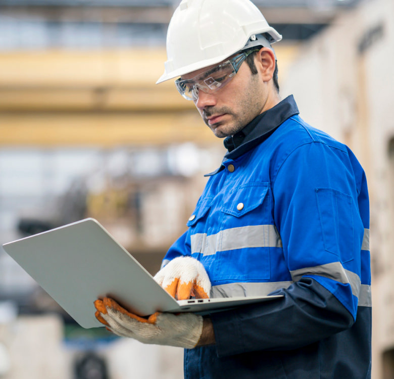 Factory Manager with hard hat and safety glasses viewing laptop on factory floor